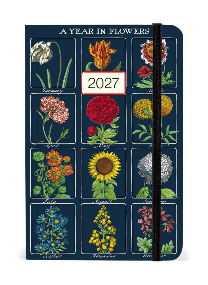A vertical 12-month floralplanner titled 'A YEAR IN FLOWERS' for 2027, featuring a dark blue cover decorated with vintage-style botanical illustrations of flowers for each month, with a black elastic closure band.