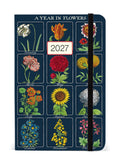 A vertical 12-month floralplanner titled 'A YEAR IN FLOWERS' for 2027, featuring a dark blue cover decorated with vintage-style botanical illustrations of flowers for each month, with a black elastic closure band.