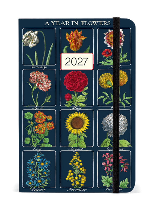 A vertical 12-month floralplanner titled 'A YEAR IN FLOWERS' for 2027, featuring a dark blue cover decorated with vintage-style botanical illustrations of flowers for each month, with a black elastic closure band.
