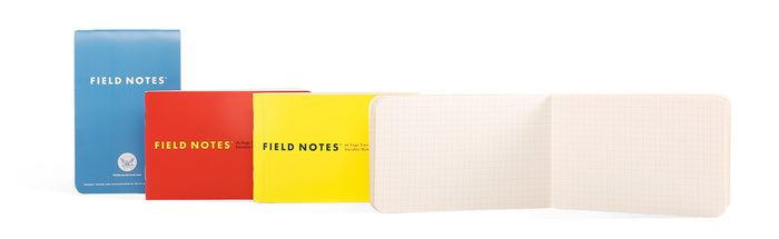 Three Field Notes notebooks in blue, red, and yellow with an open notebook on a white background.