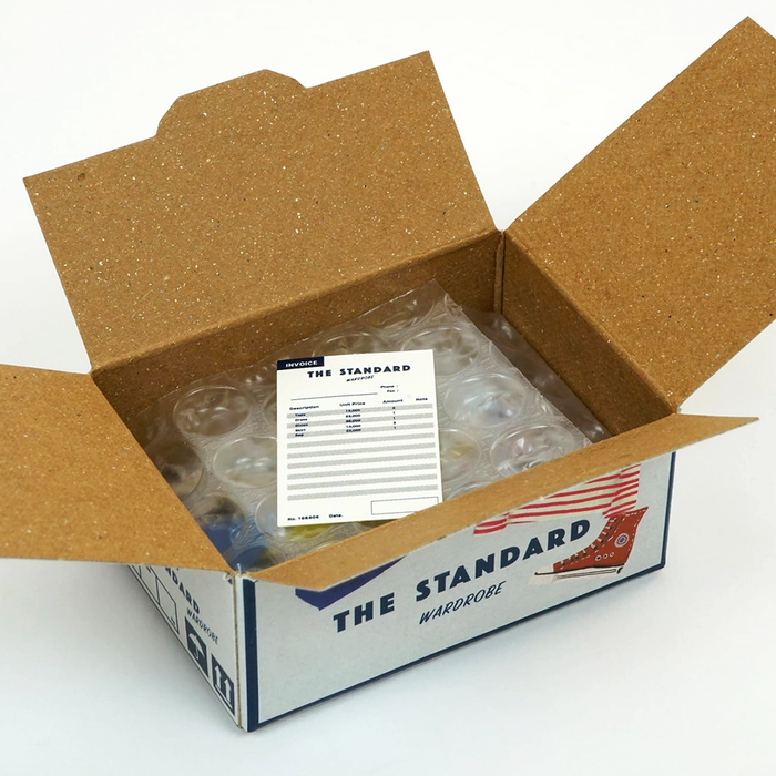 Open cardboard box with 'The Standard Wardrobe' label with packaging and invoice inside on a white background