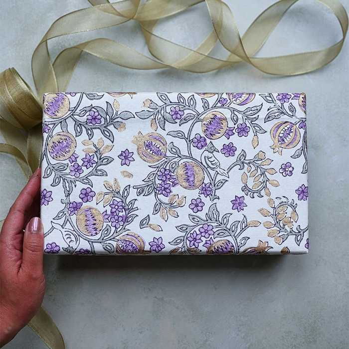 Block Printed indigo and gold pomegranate pattern with  green leaves used to wrap a gift. Shown with a hand and gold ribbon.