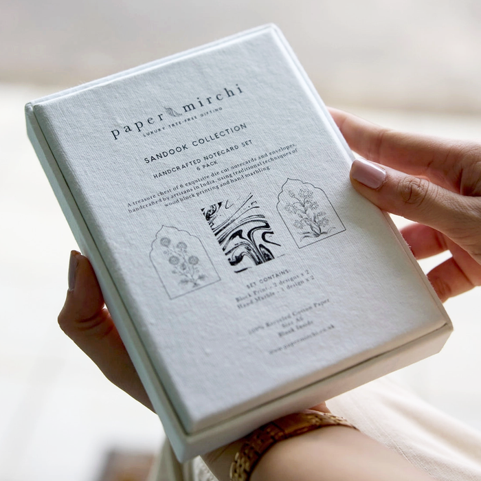 Hand holding a 'paper mirchi' sandook collection box set against a neutral background