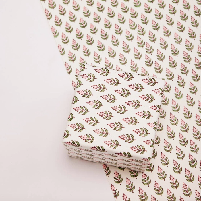 paper with repeating pink and green floral pattern on a white background with one flat sheet and a box wrapped with the same paper