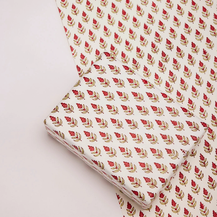 Paper with red and green floral and leaf repeat pattern with one flat sheet and a wrapped box with the same pattern