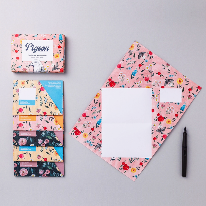 Pigeon floral stationery set- 5 cards with 3 different colorways, one displayed open,  product packaging, and a pen on a gray background