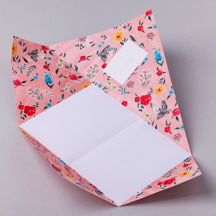 Colorful origami folded letter shown open with floral-themed design on a light gray background