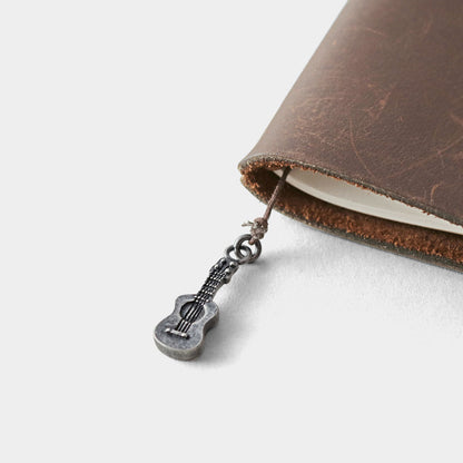 Brown leather TRAVELER'S NOTEBOOK with ukelele charm on a white background
