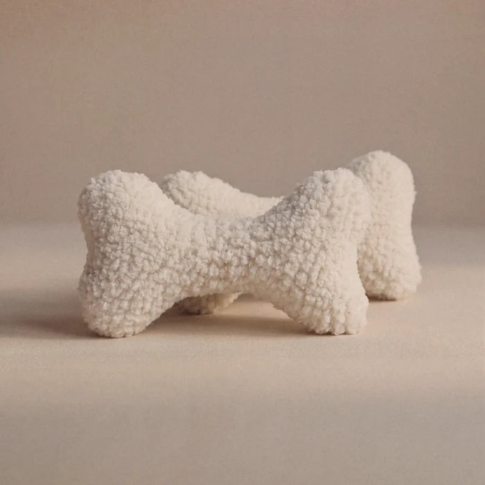 Two textured wool bone-shaped pet pillows in an off-white bouclé wool fabric, displayed on a neutral beige background.
