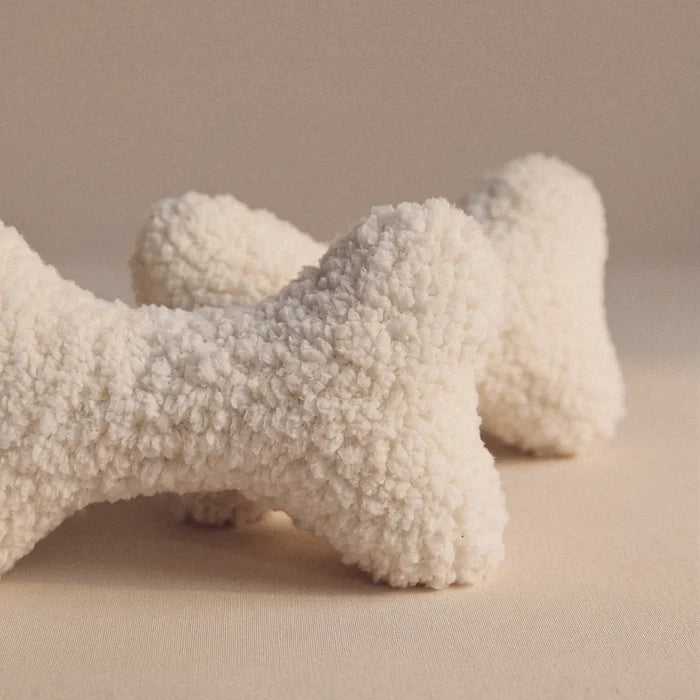 Two textured wool bone-shaped pet pillows in an off-white bouclé wool fabric, displayed on a neutral beige background.
